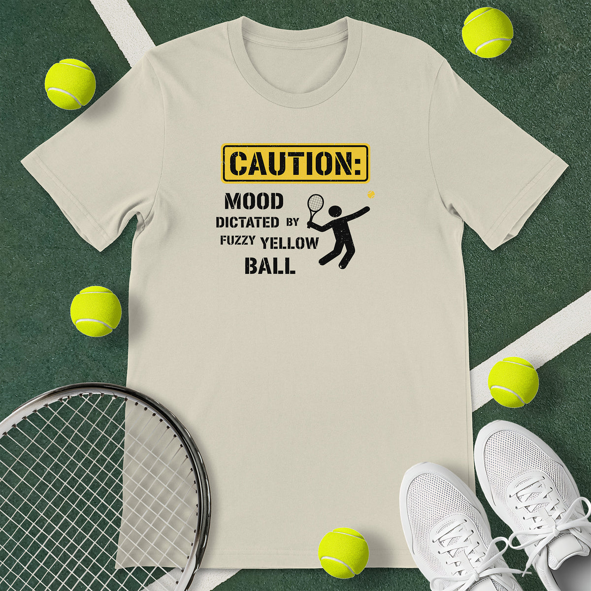 Off-white t-shirt with the text 'CAUTION: MOOD DICTATED BY FUZZY YELLOW BALL' and a graphic of a person serving.