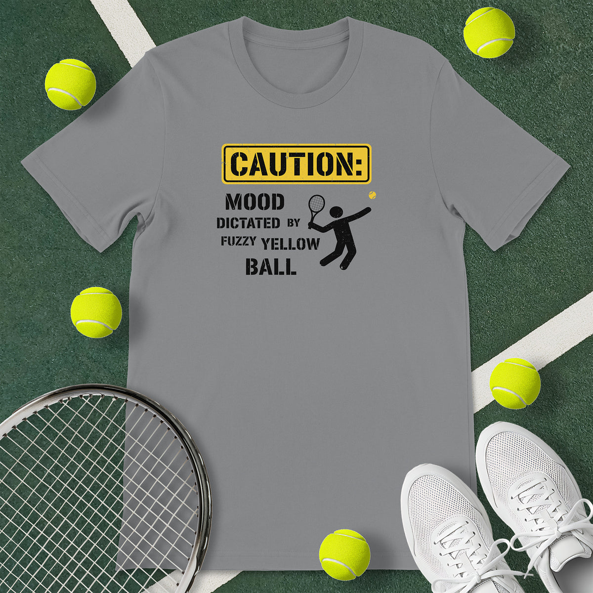 Grey t-shirt with the text 'CAUTION: MOOD DICTATED BY FUZZY YELLOW BALL' and a graphic of a person serving.