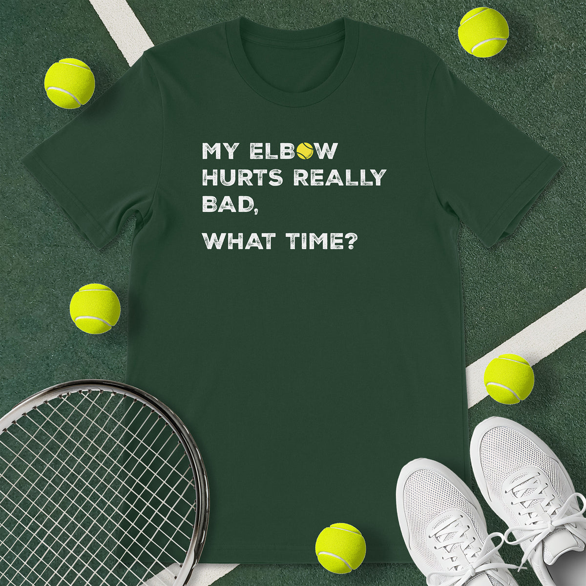 Forest green t-shirt with the text 'MY ELBOW HURTS REALLY BAD, WHAT TIME?' and a graphic of a tennis ball.