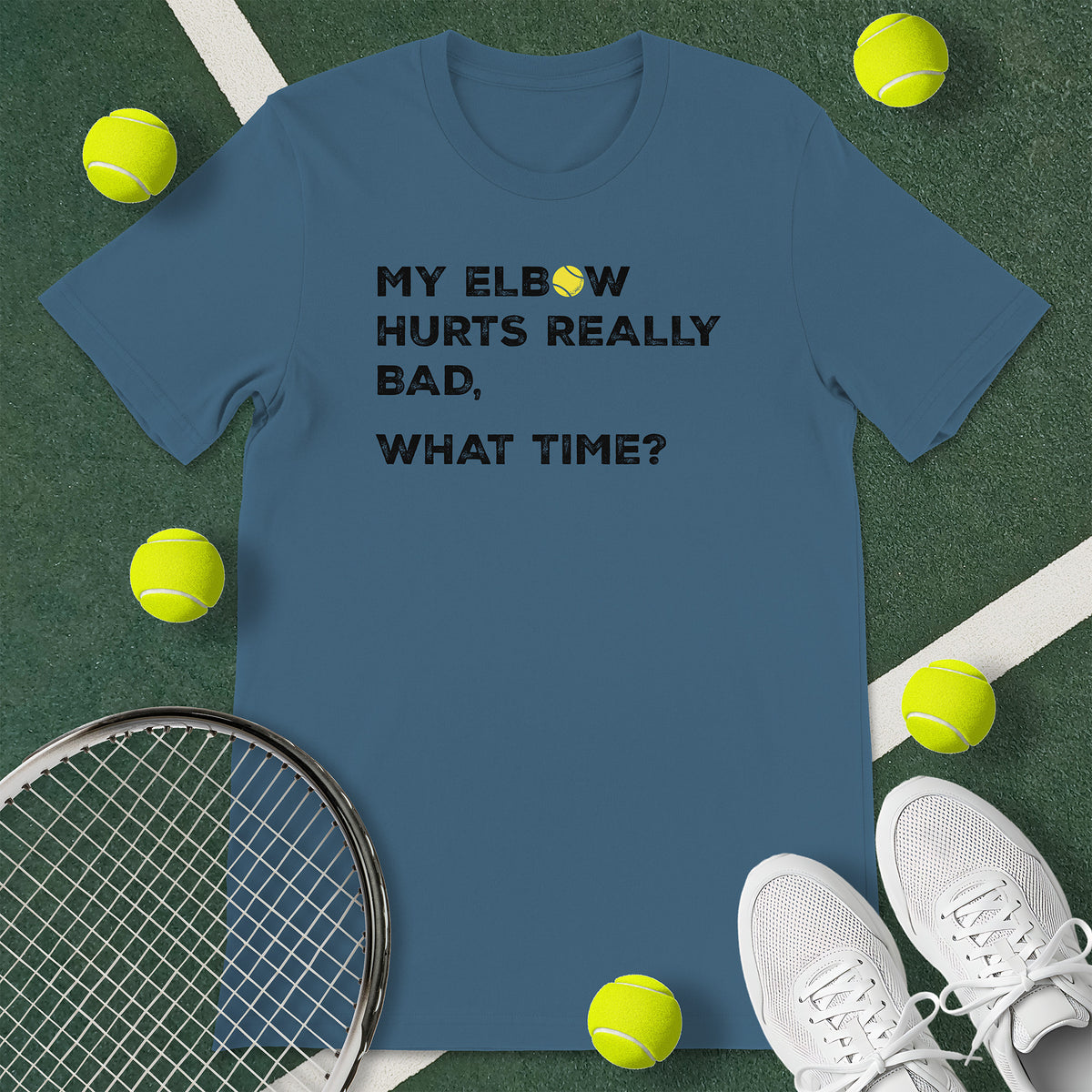 Indigo blue t-shirt with the text 'MY ELBOW HURTS REALLY BAD, WHAT TIME?' and a graphic of a tennis ball.